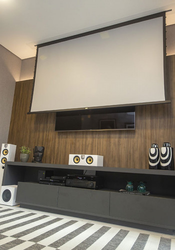 Quando a tela de 106” sobe, revela o TV de 65” montado sobre o painel de parede