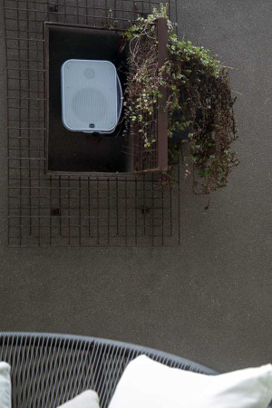 Detalhe de uma das caixas outdoor: elas foram montadas em nichos da parede, com ess discreta grade metálica que também serve de suporte para as plantas decorativas.
