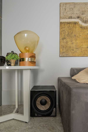 Posicionado entre a mesa de canto e o sofá, o subwoofer fica bem discreto na sala.