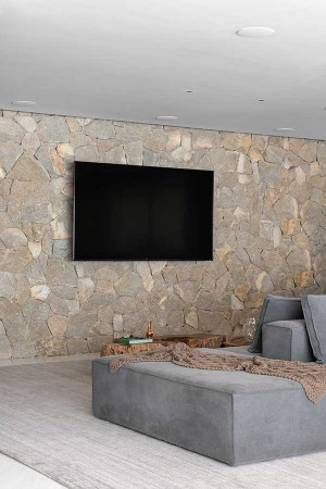 No home theater da área de lazer, a TV foi montada sobre a parede revestida de pedra.