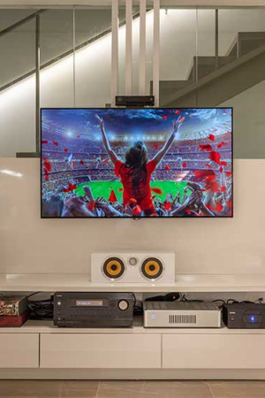 Detalhe de um sistema de home theater com TV, receiver e caixas acústicas.