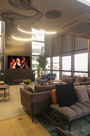 Visão ampla da sala de home theater, ao lado do living, com uma das caixas acústicas no teto.