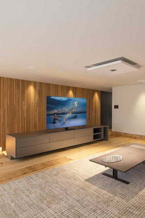 Vista da sala íntima, com TV de 75” e todas as caixas embutidas no teto.