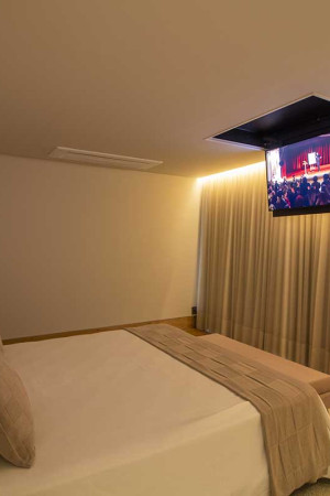 Na suíte e em outros ambientes da casa, as TVs foram montadas em flaps embutidos no teto.