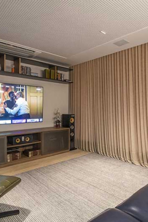 Detalhe do home theater, com TV, som, luzes e cortinas controlados pelo smartphone.