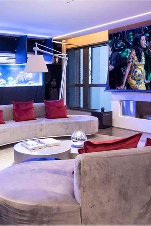 Vista do living com assentos laterais e outra tela de 120”; ao fundo, um aquário.