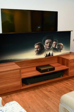 Aqui, uma sala íntima com a tela (106”) embutida no móvel e sobreposta à TV de 70”.