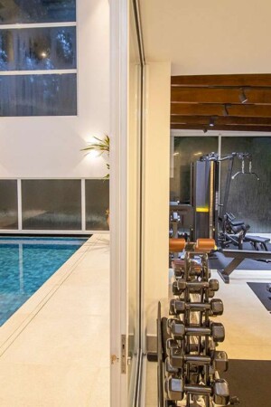 A academia, ao lado da piscina, também ganhou uma TV; o som é reproduzido por uma soundbar.