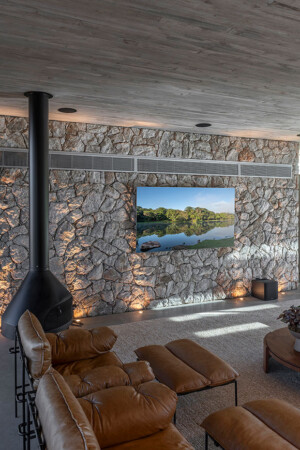 No espaço gourmet, a TV também foi montada sobre a parede de pedra, com subwoofer no piso e as três caixas frontais na laje.