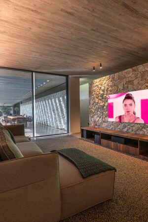 Vista do home theater, com caixas frontais montadas no móvel baixo e as surround do tipo on-wall nas laterais do sofá.